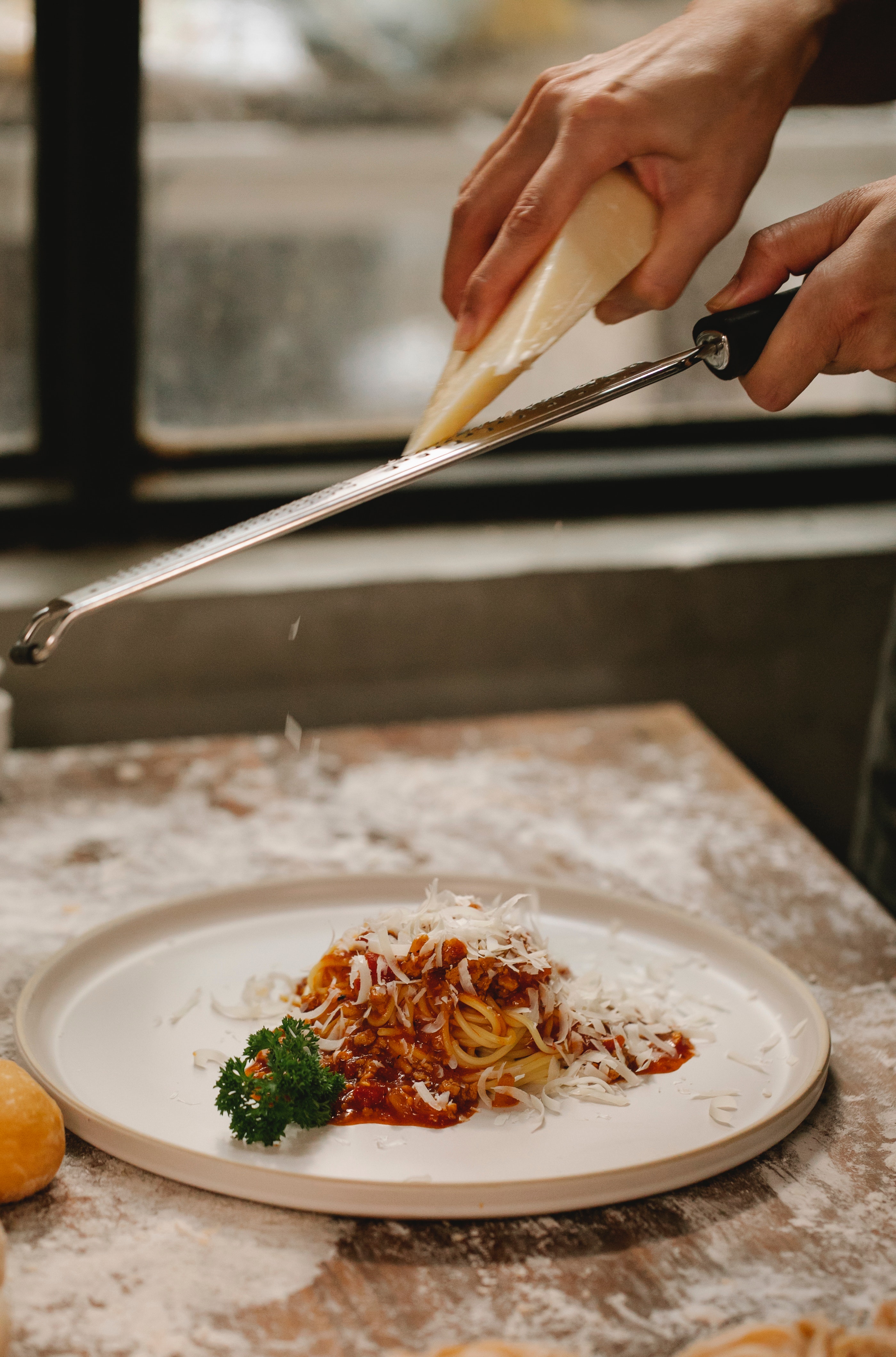 Woman grating parmesan cheese over a plate of pasta