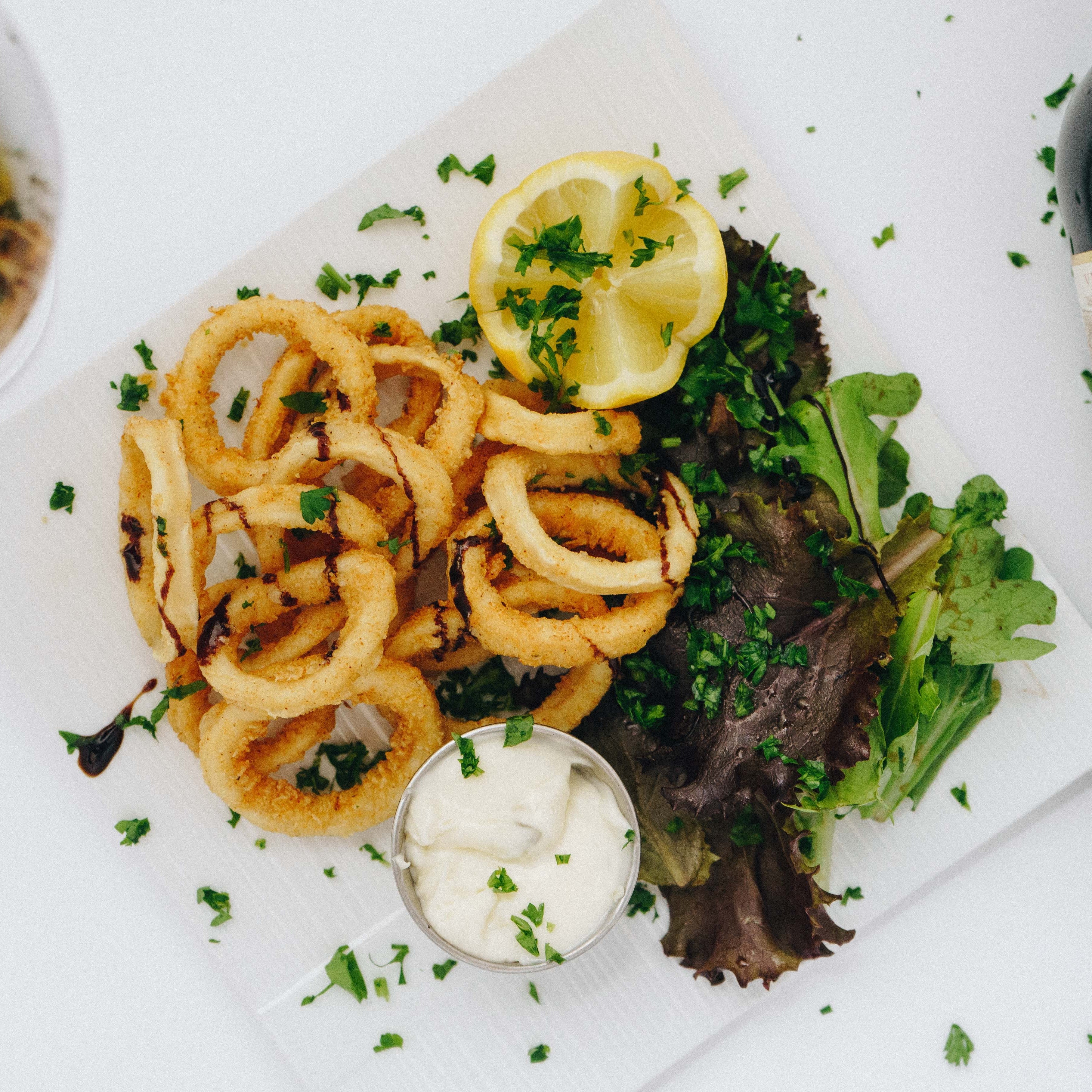 Overhead shot of a plate of calamari fritti served with green, dip and a lemon wedge