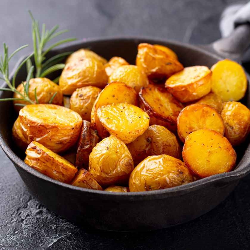 Close up shot of roasted potatoes in a cast iron skillet garnished with a couple sprigs of rosemary