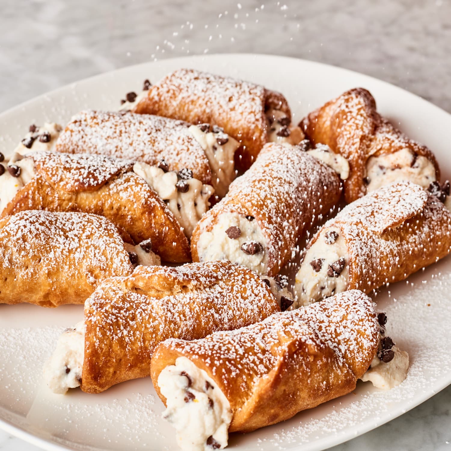 Close up shot of a plate of chocolate chip cannolis dusted with a generous amount of powdered sugar