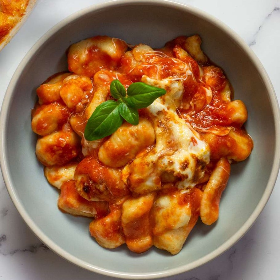 Overhead shot of gnocchi in tomato sauce with a dollop of cheese and garnished with a few leaves of basil