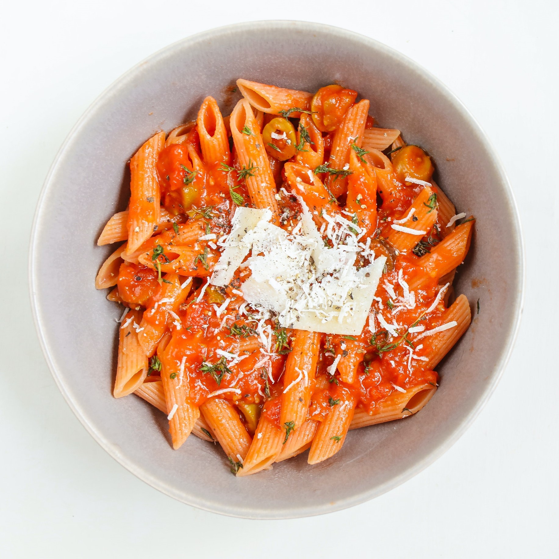 Overhead shot of penne pasta in tomato sauce topped with shredded cheese