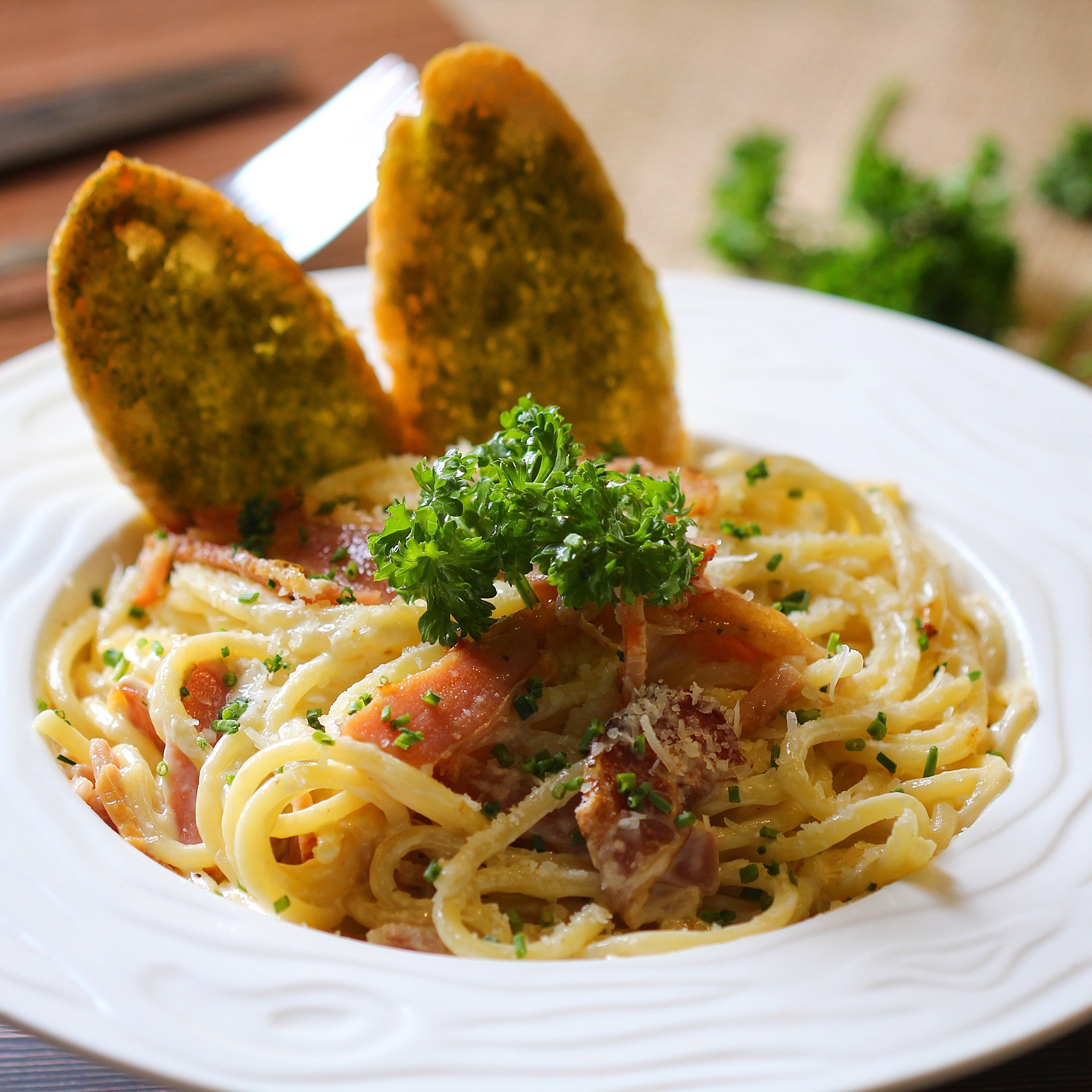 Close up shot of a plate of spaghetti served with two pieces of garlic bread and garnished with curly parsley