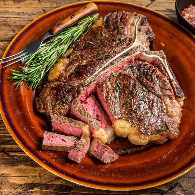 Overhead shot of a plate of grilled rib-eye steak served with a few sprigs of fresh rosemary