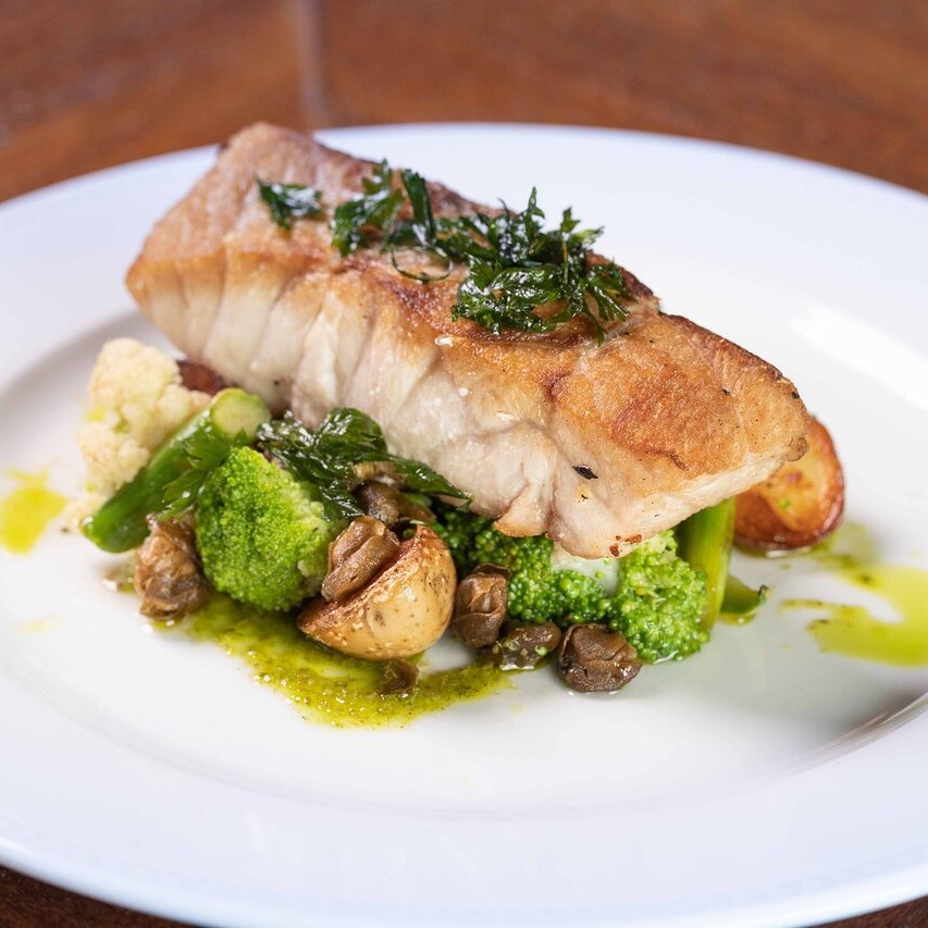 Close up shot of a sample fish dish. A panfried salmon fillet served on a bed of veggies including broccoli, asparagus, mushroom and cauliflower