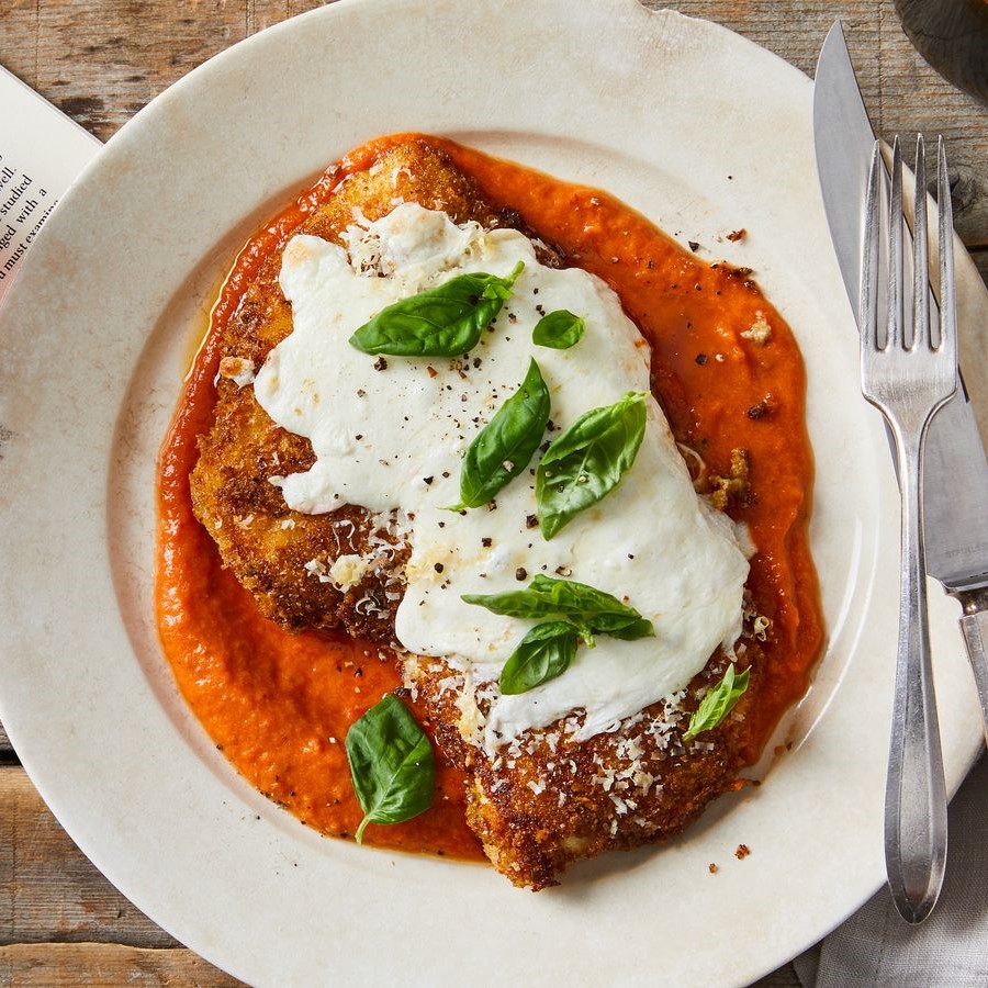 Overhead shot of fried breaded chicken fillet topped with melted mozarella cheese on a bed of marinara sauce and garnished with a few leaves of basil